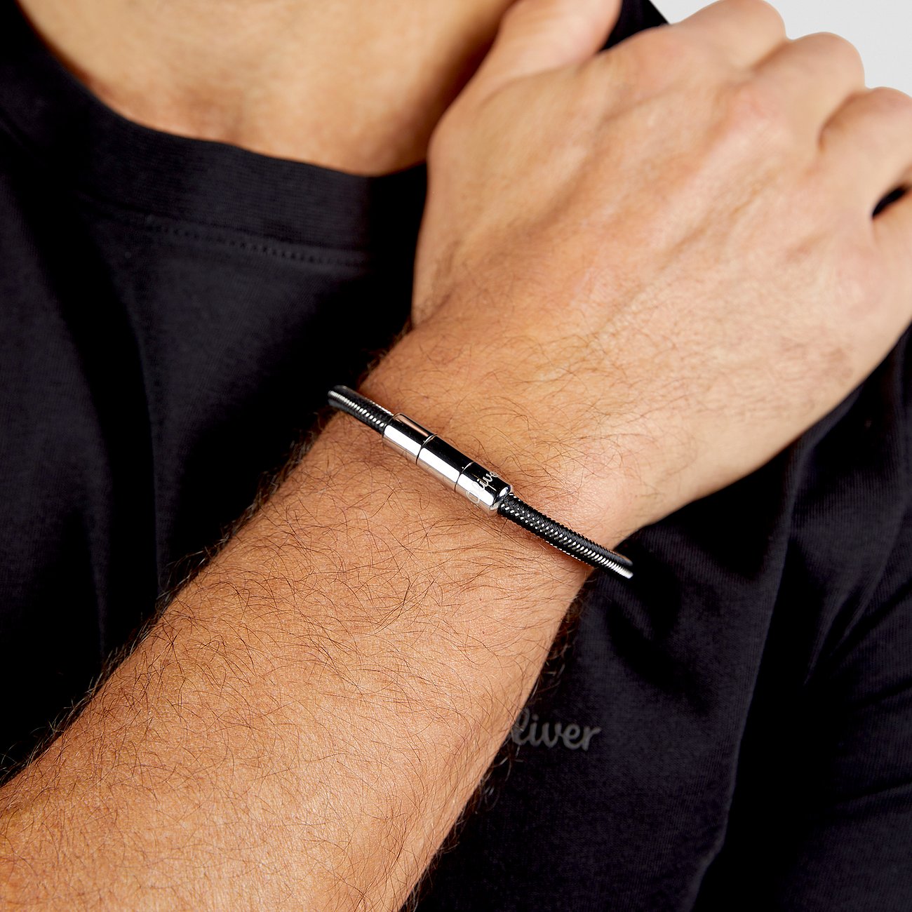 Ein s.Oliver Herren-Armband aus Edelstahl am Handgelenk eines Mannes, mit einem silbernen Mittelstück.