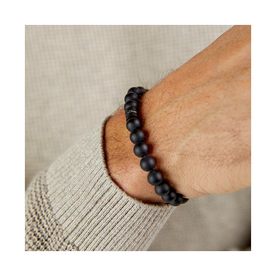 Un bracelet s.Oliver en pierres noires avec un pendentif de marque, porté au poignet d'un homme.