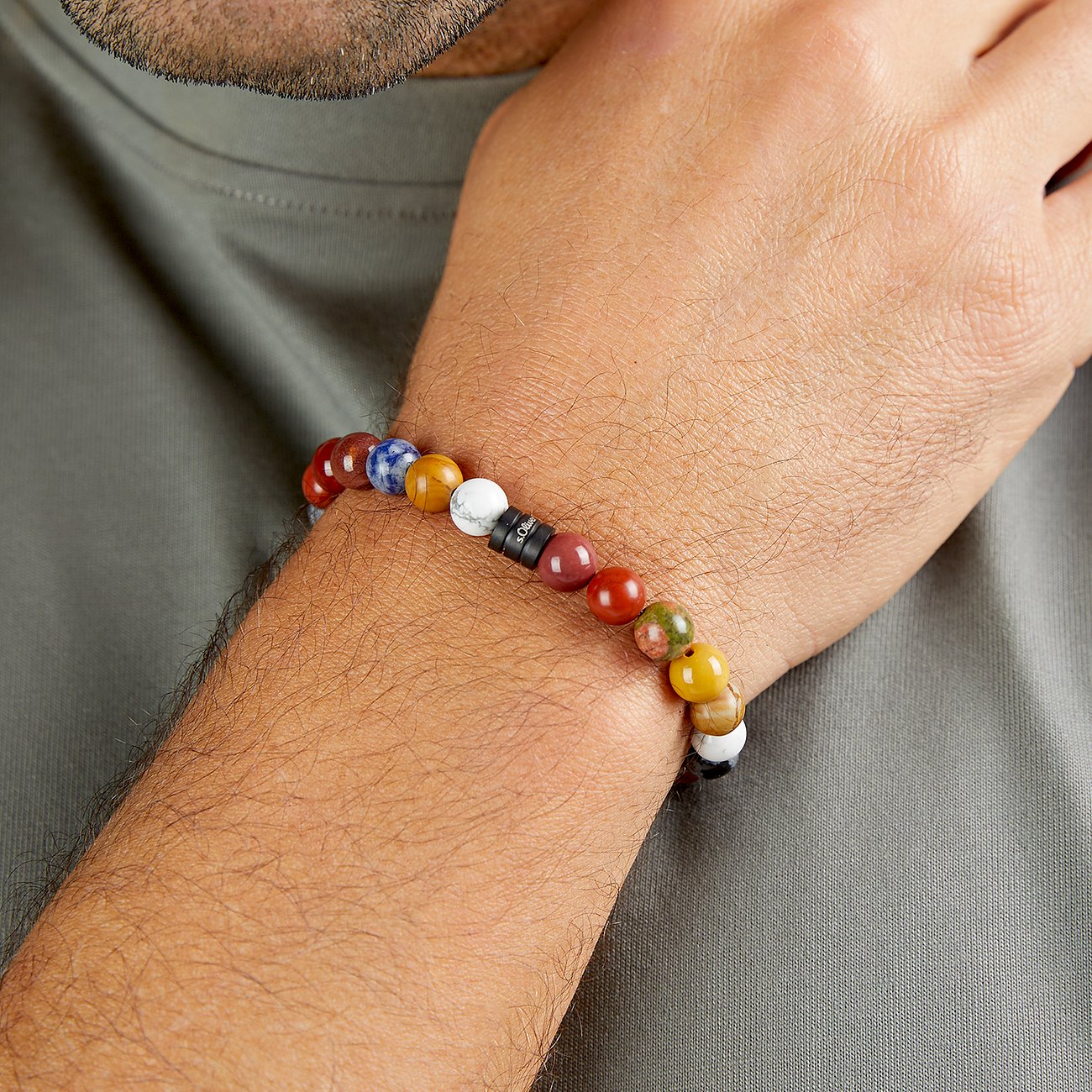 Un bracelet homme s.Oliver à perles de pierre blanches, bleues, jaunes et rouges, porté au poignet d'un homme.