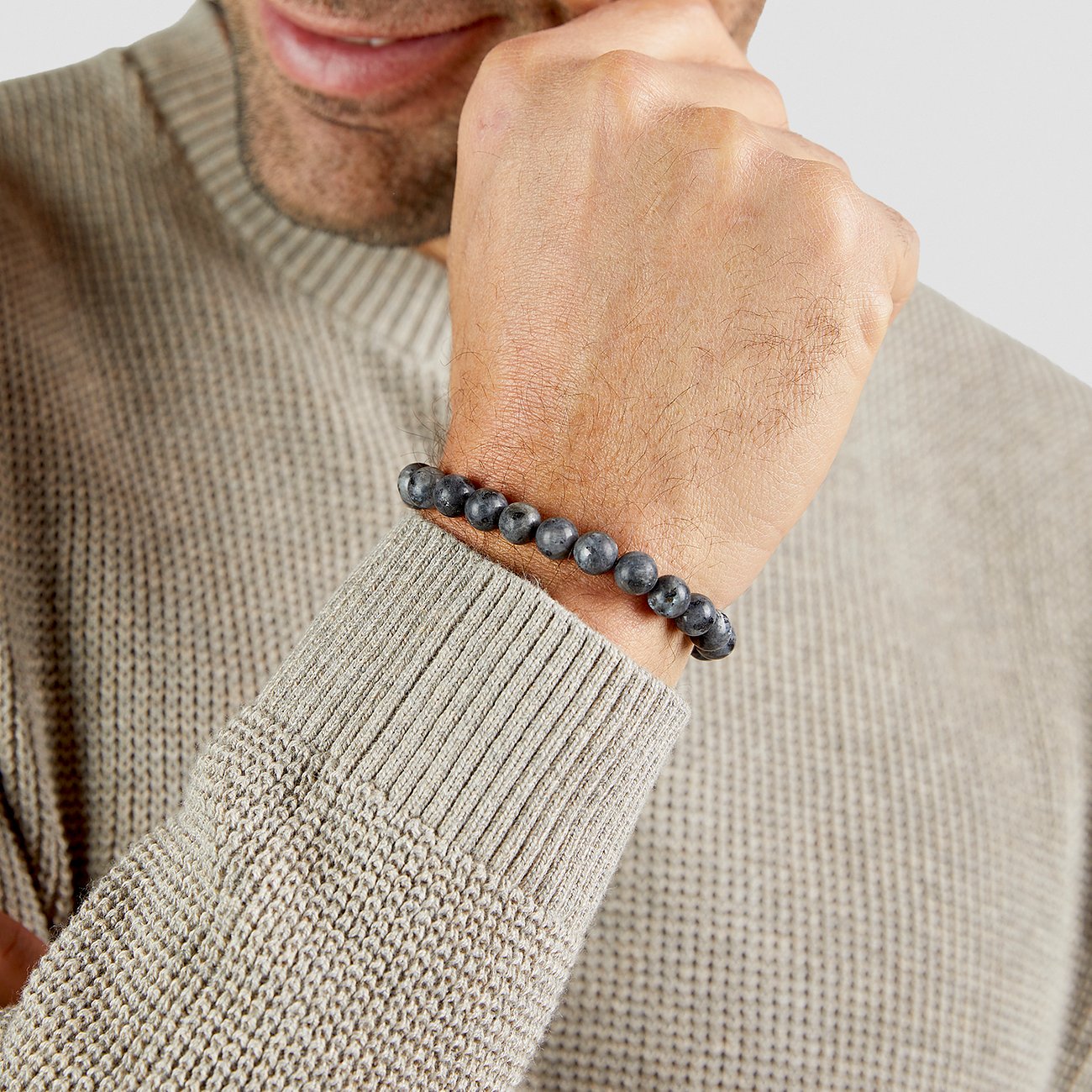 Al polso di un uomo con un maglione beige, si vede un bracciale s.Oliver con pietre scure.
