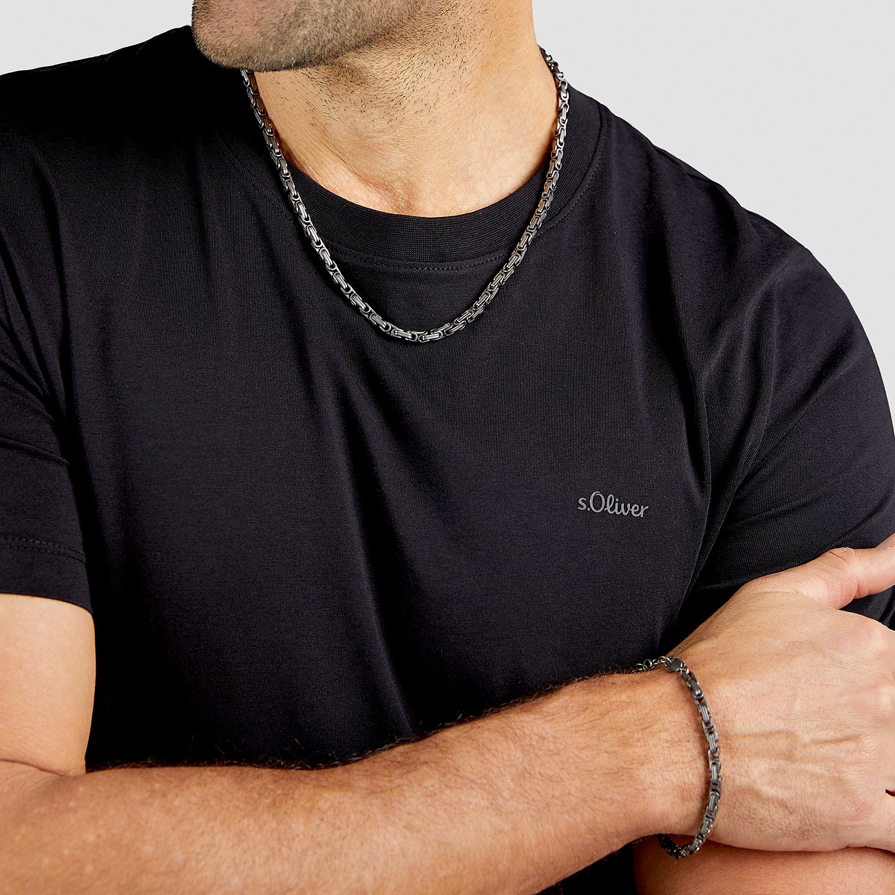 Ein Mann trägt eine s.Oliver Halskette und ein passendes Armband aus Edelstahl über einem schwarzen T-Shirt.
