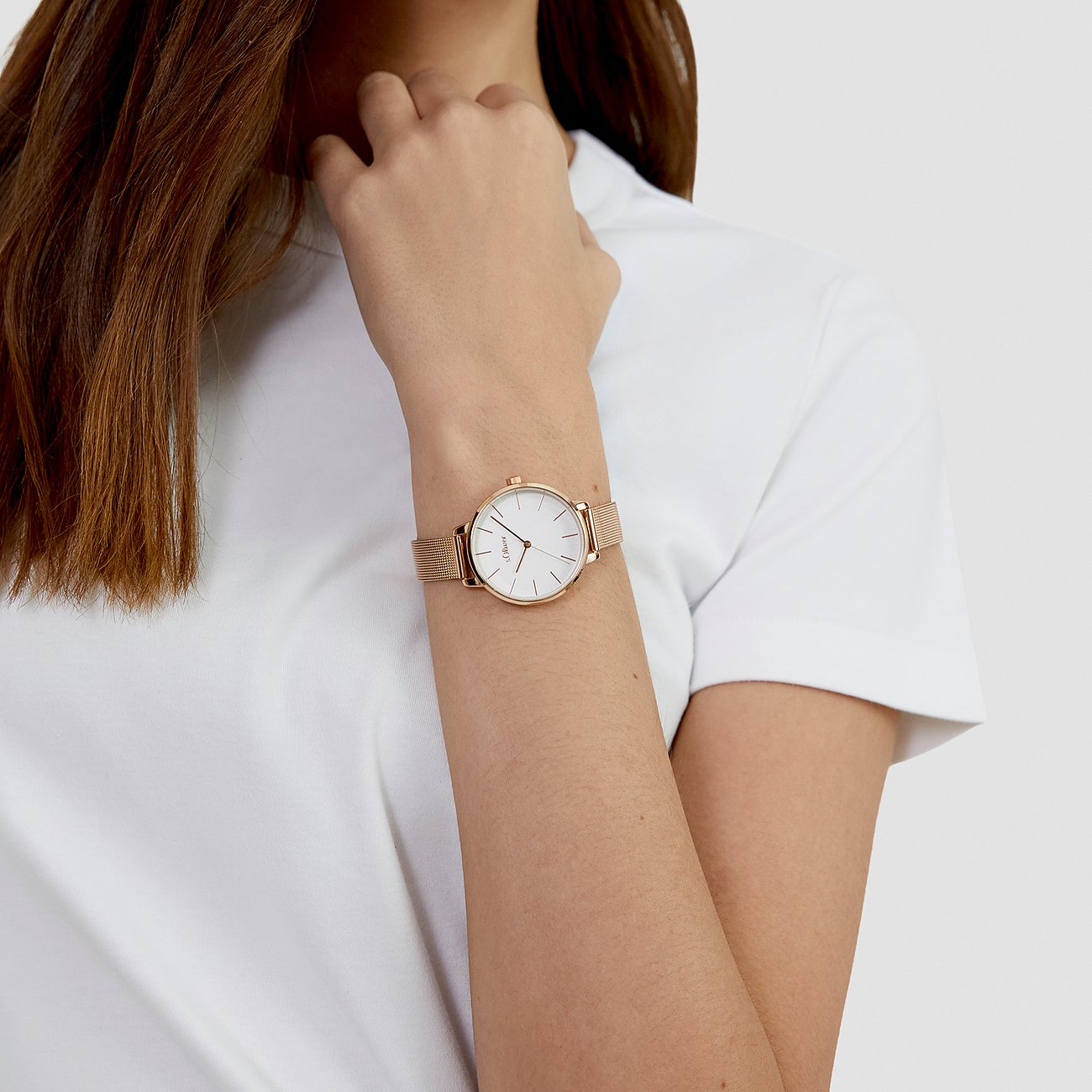 Gros plan d'une montre femme s.Oliver en métal doré rose avec cadran blanc au poignet sur fond blanc.