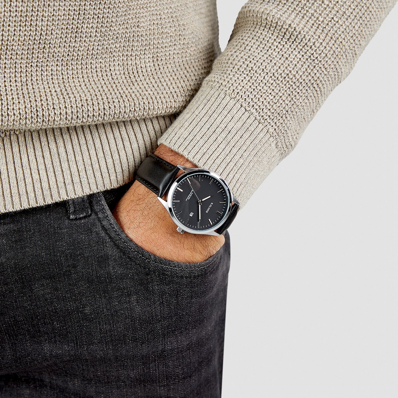 Ein Mann trägt eine s.Oliver Herrenuhr aus Metall mit schwarzem Zifferblatt und Lederarmband.