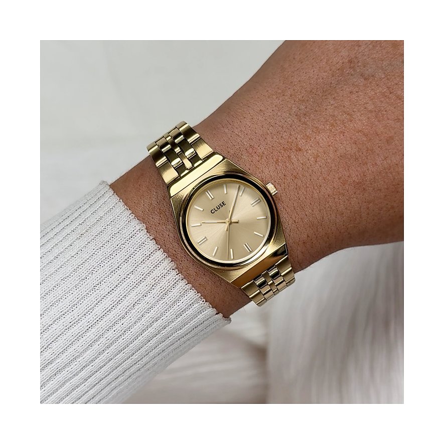 Am Handgelenk getragene goldene Cluse Damenuhr aus Edelstahl mit ovalem Zifferblatt und glänzendem Armband.