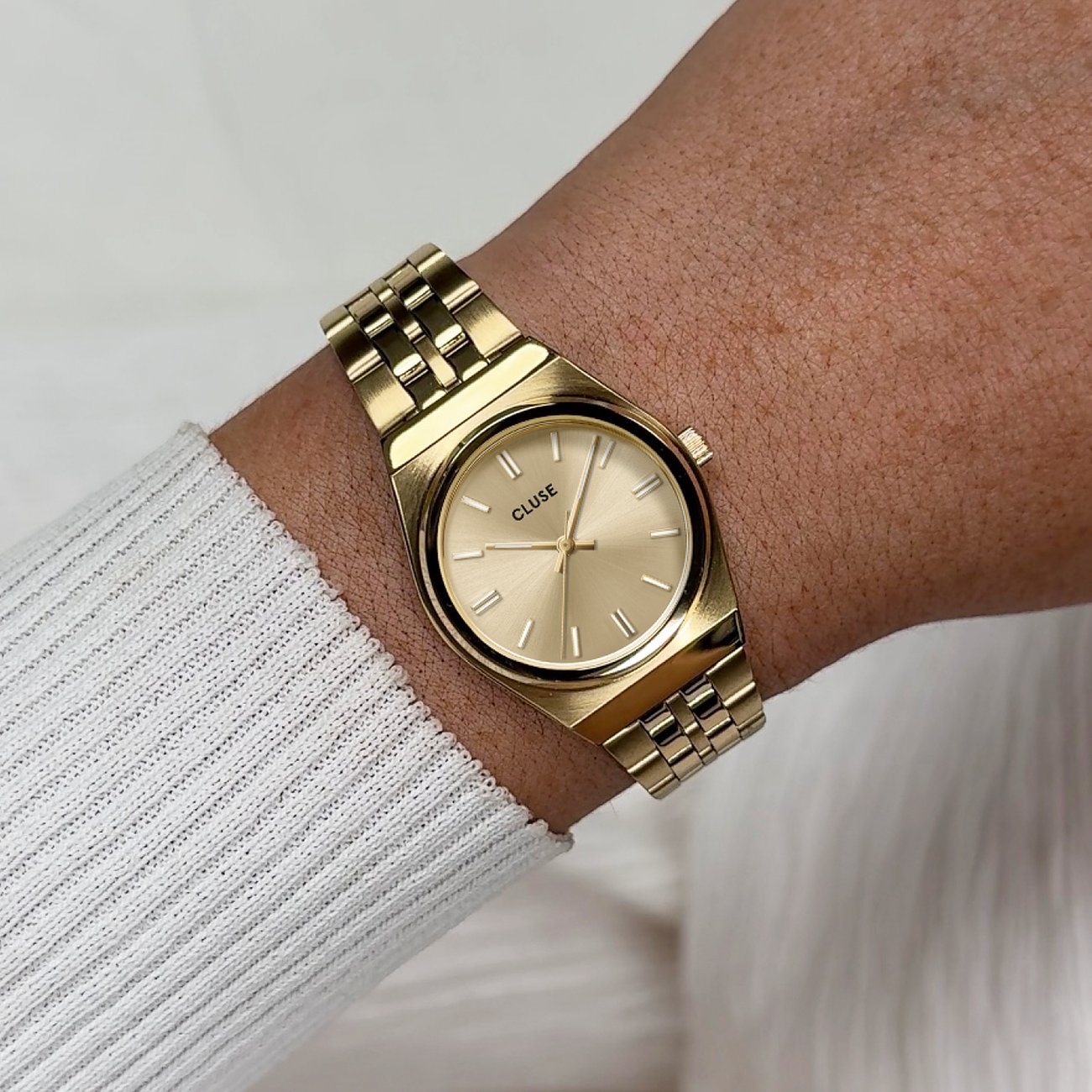 Am Handgelenk getragene goldene Cluse Damenuhr aus Edelstahl mit ovalem Zifferblatt und glänzendem Armband.