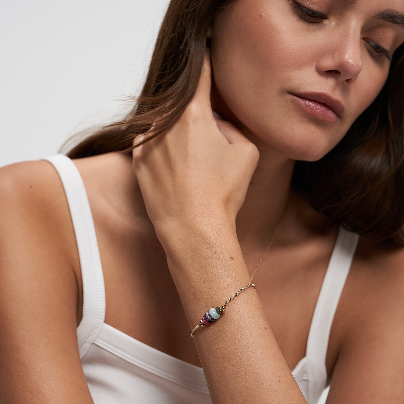 Délicat bracelet Tamaris en acier inoxydable doré avec trois perles colorées en aventurine au poignet d'une mannequin.
