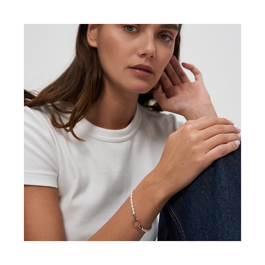 En kvinna bär ett Tamaris armbandsur i rostfritt stål med pärlor, elegant vilande kring hennes handled.