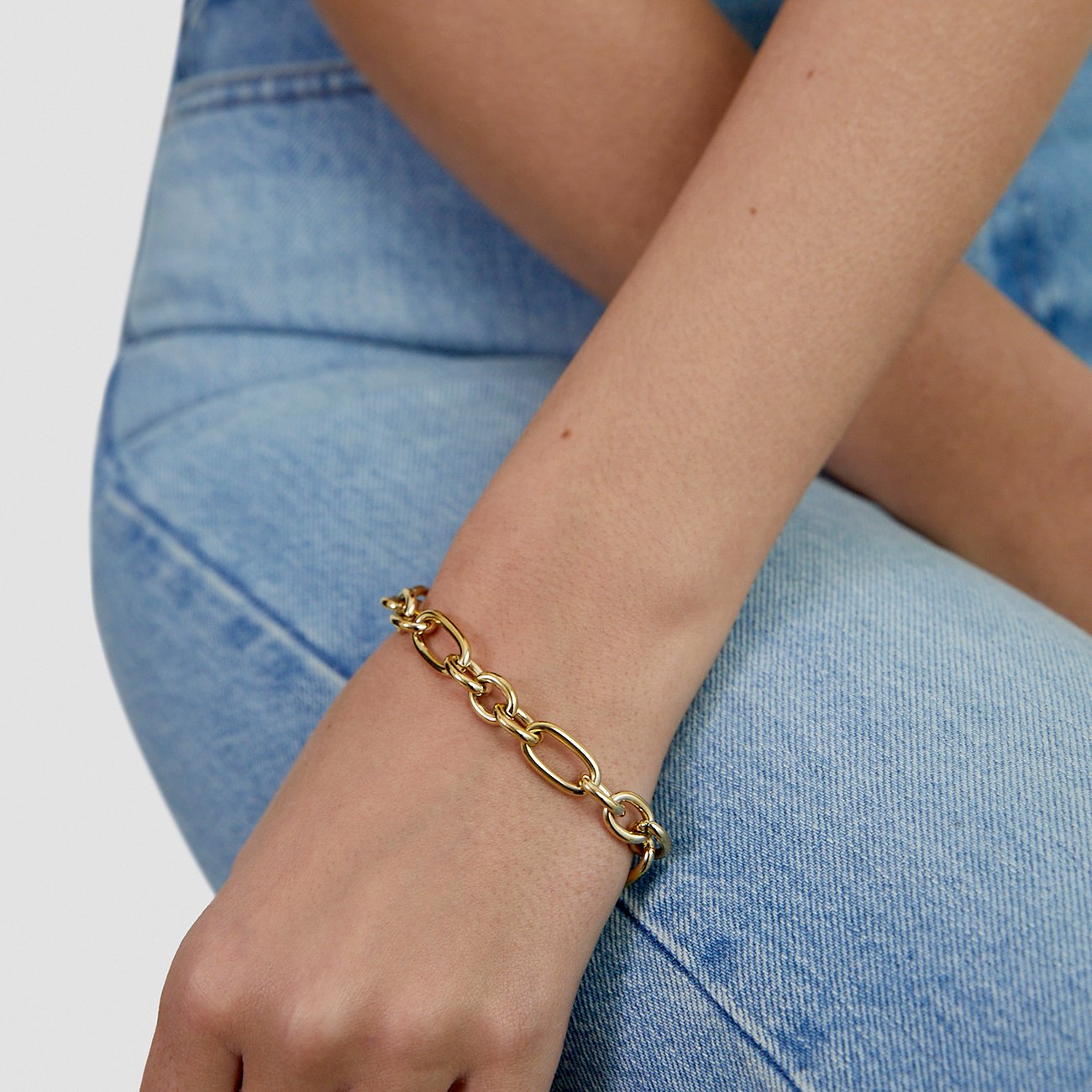Goldfarbenes Tamaris Armband aus Edelstahl mit großen ovalen Gliedern am Handgelenk einer Person mit Jeanshose.