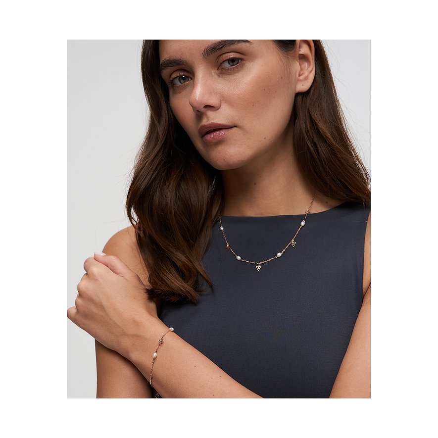 Een vrouw draagt een Tamaris roestvrijstalen ketting met parels en klaverhangers, plus een bijpassende armband.