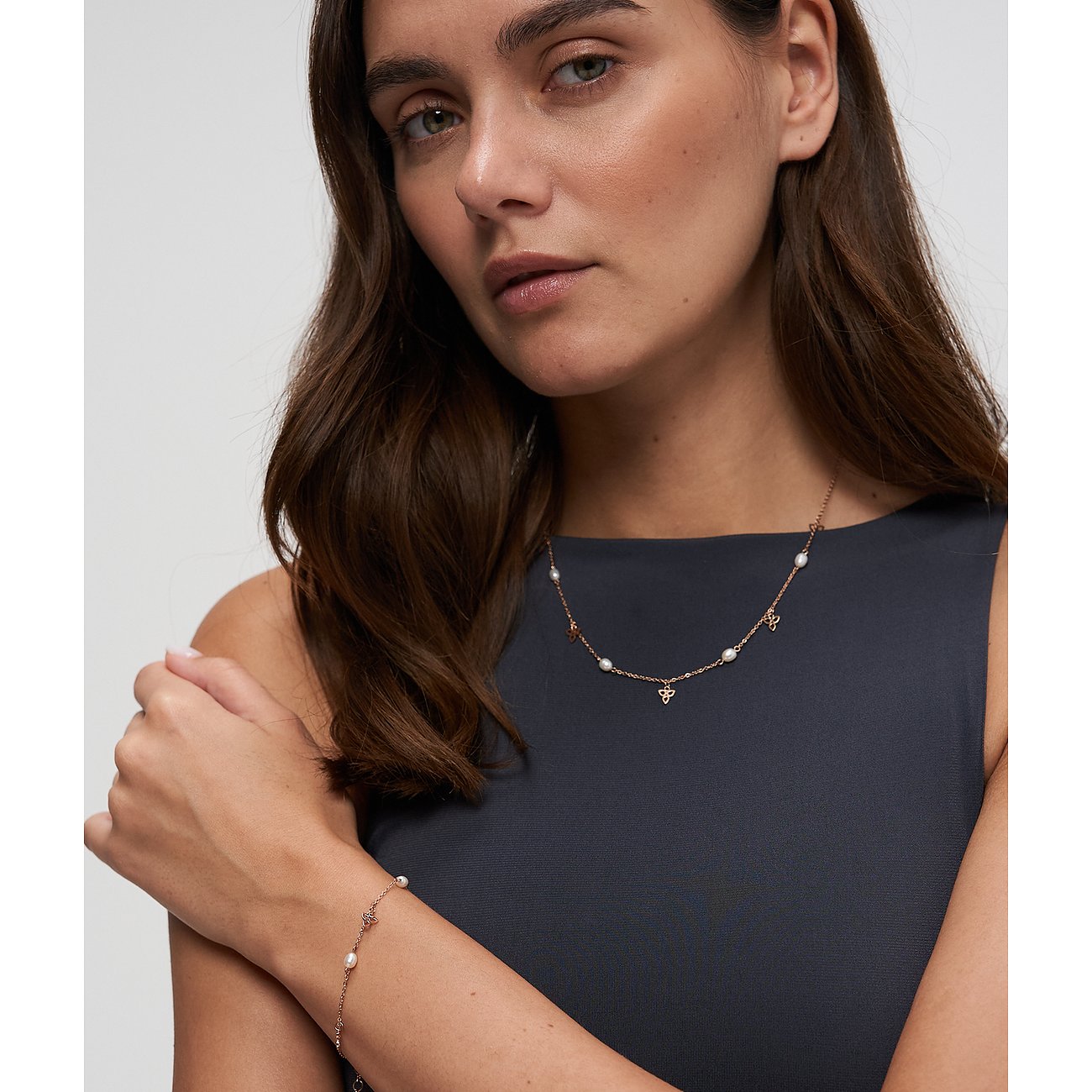 Een vrouw draagt een Tamaris roestvrijstalen ketting met parels en klaverhangers, plus een bijpassende armband.