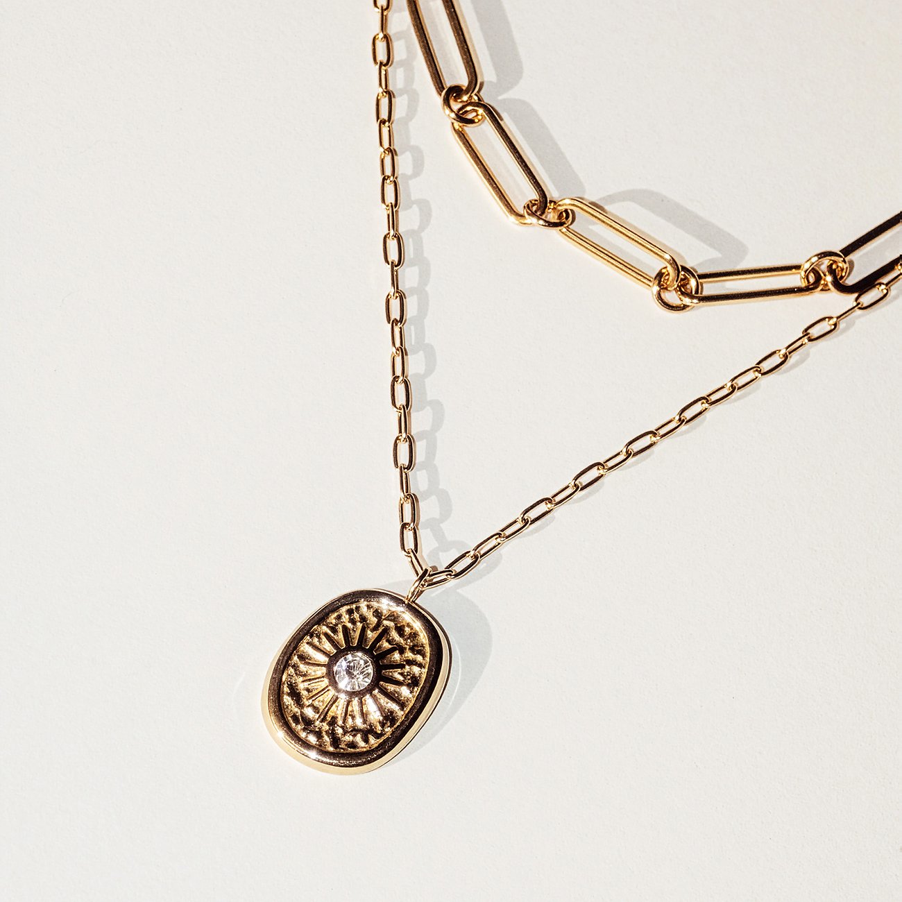 Close-up einer Tamaris Halskette aus goldfarbenem Edelstahl mit zwei Ketten und einem ovalen Anhänger mit Zirkonia-Stein.