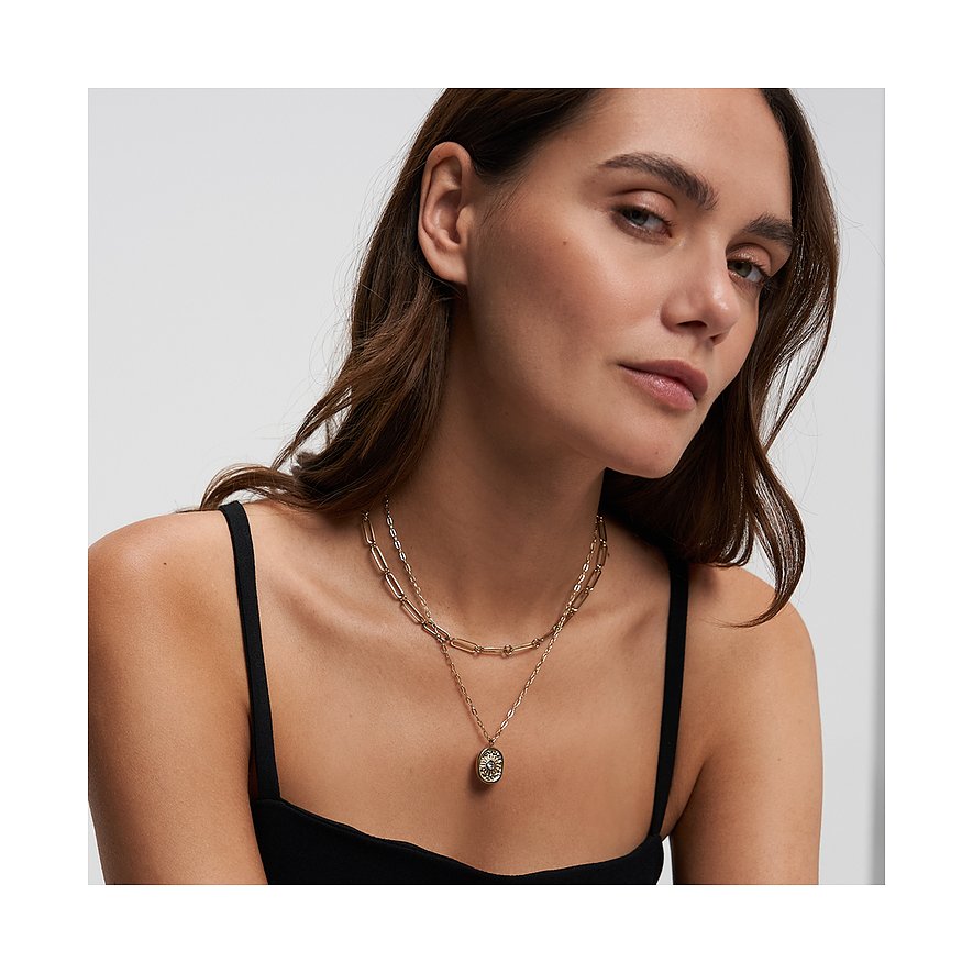 Eine Frau trägt ein Tamaris Schmuck-Set aus goldenem Edelstahl mit einem Zirkonia-besetzten ovalen Anhänger.