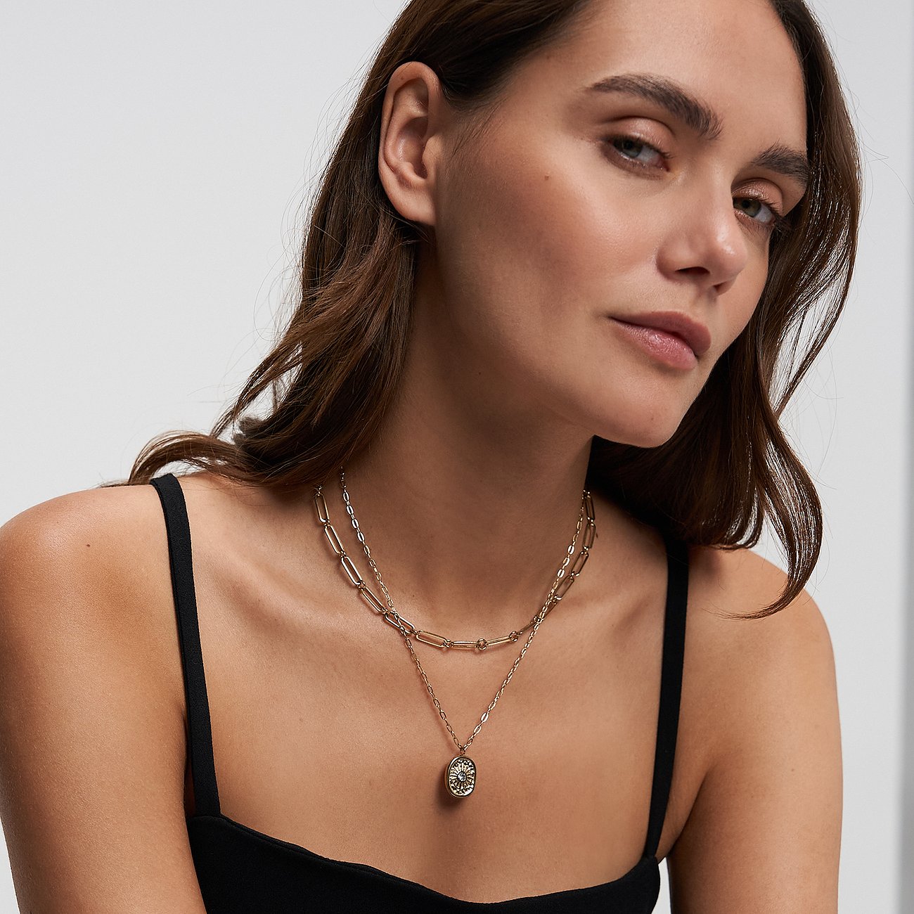 Eine Frau trägt ein Tamaris Schmuck-Set aus goldenem Edelstahl mit einem Zirkonia-besetzten ovalen Anhänger.