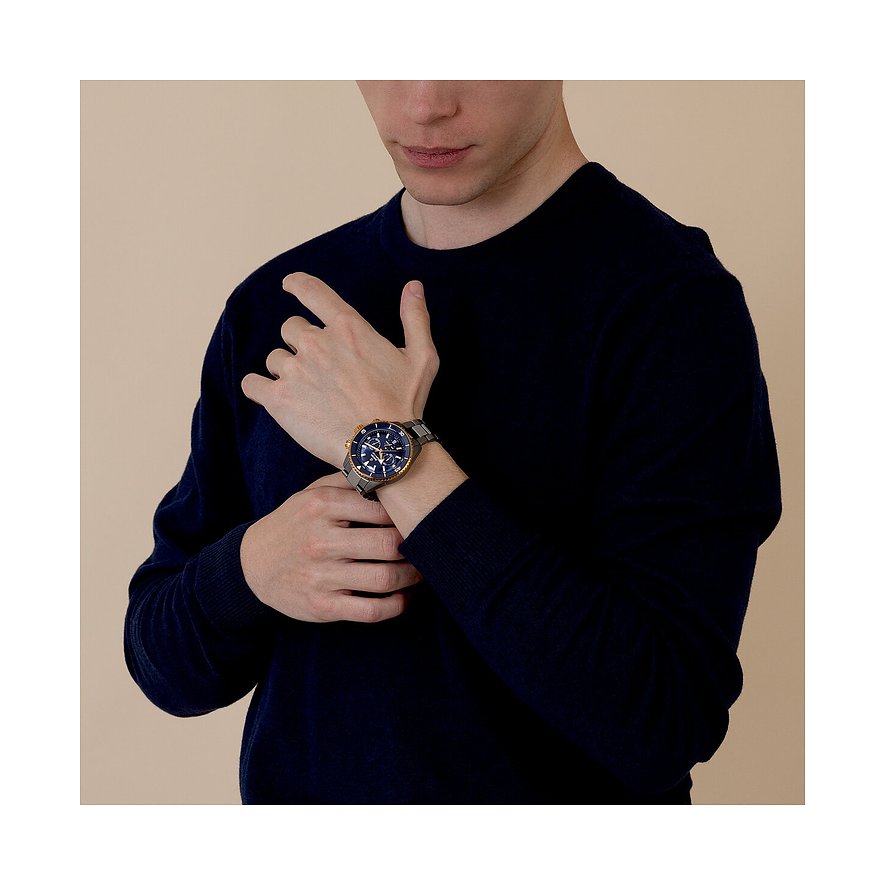 Ein Mann trägt eine Rado Herrenuhr aus blauem und goldenem Keramik am Handgelenk und hält seinen Arm.