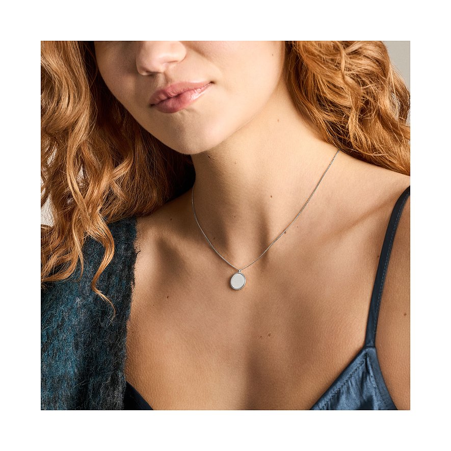 Gros plan d'une femme en haut marine, portant un collier Fossil en acier inoxydable avec un pendentif rond.