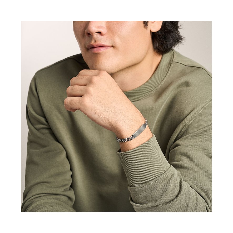 En man tittar framåt, bär det silverfärgade Fossil armbandsuret i rostfritt stål med länkar och graveringsplatta.