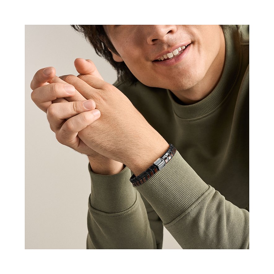Ein lächelnder Mann trägt ein Fossil Armband aus geflochtenem Leder in Schwarz und Braun mit einer Edelstahl-Schließe.