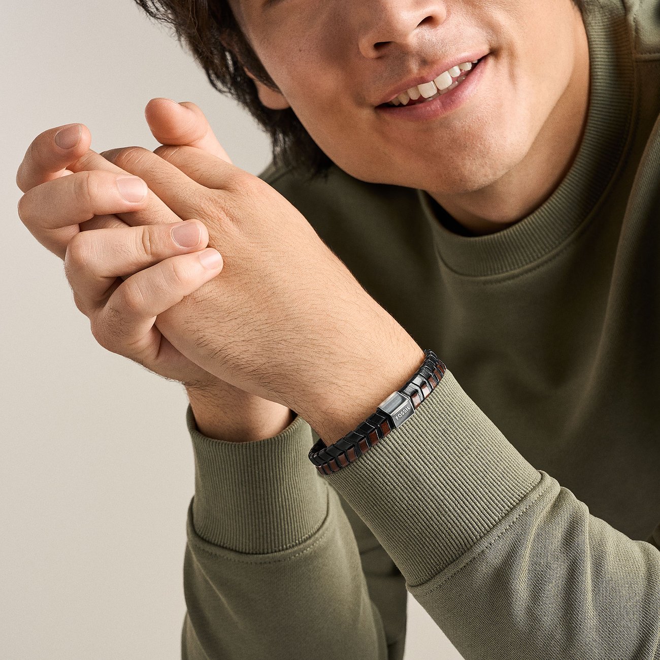 Ein lächelnder Mann trägt ein Fossil Armband aus geflochtenem Leder in Schwarz und Braun mit einer Edelstahl-Schließe.