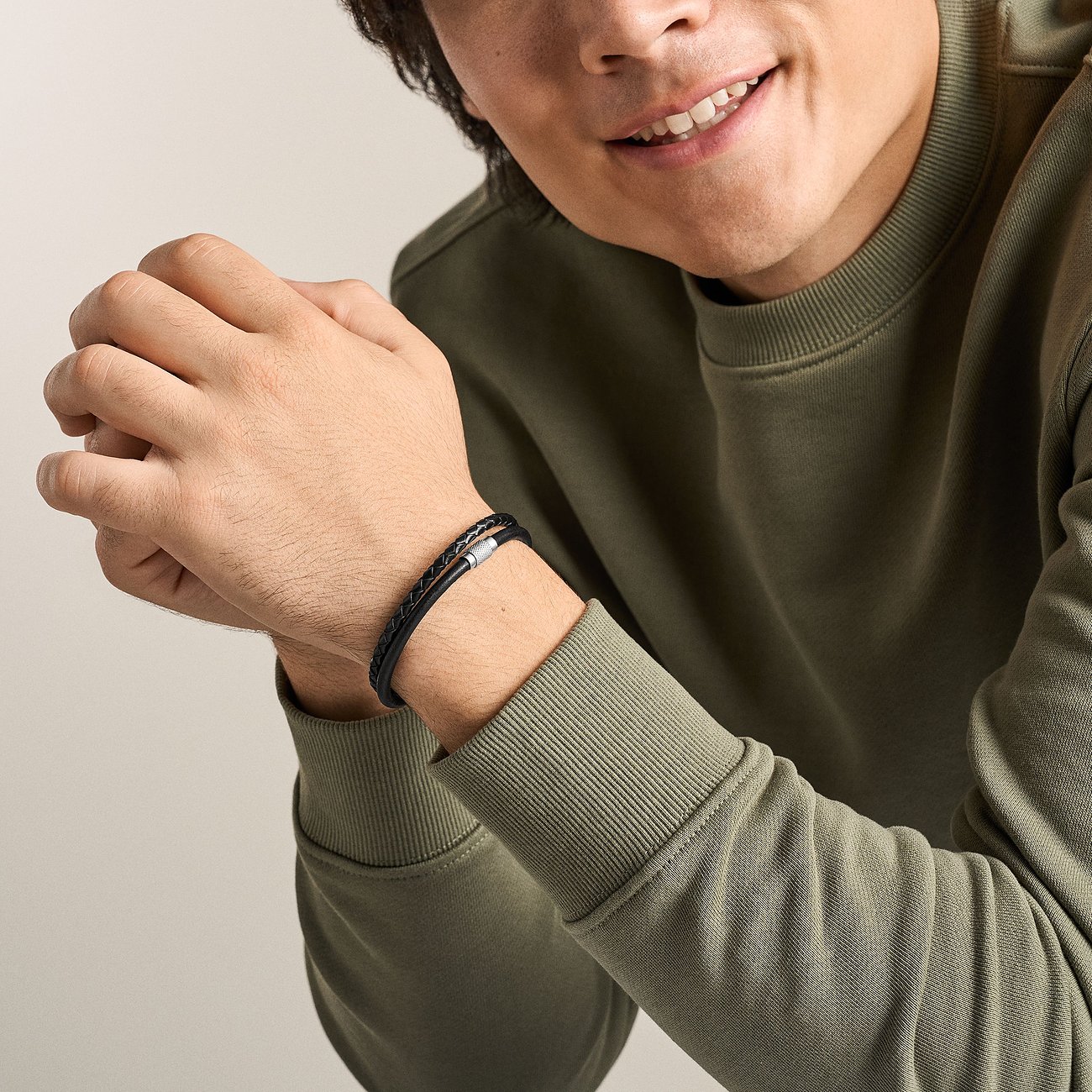 Lächelnder Mann trägt Fossil Armband aus geflochtenem schwarzem und braunem Leder mit Edelstahlverschluss am Handgelenk.