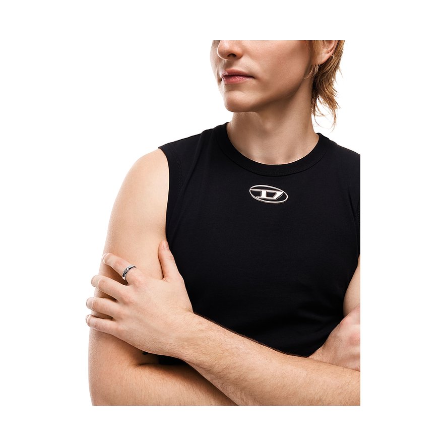 En Diesel-ring af rustfrit stål på hånden af en person med krydsede arme og sort tanktop.