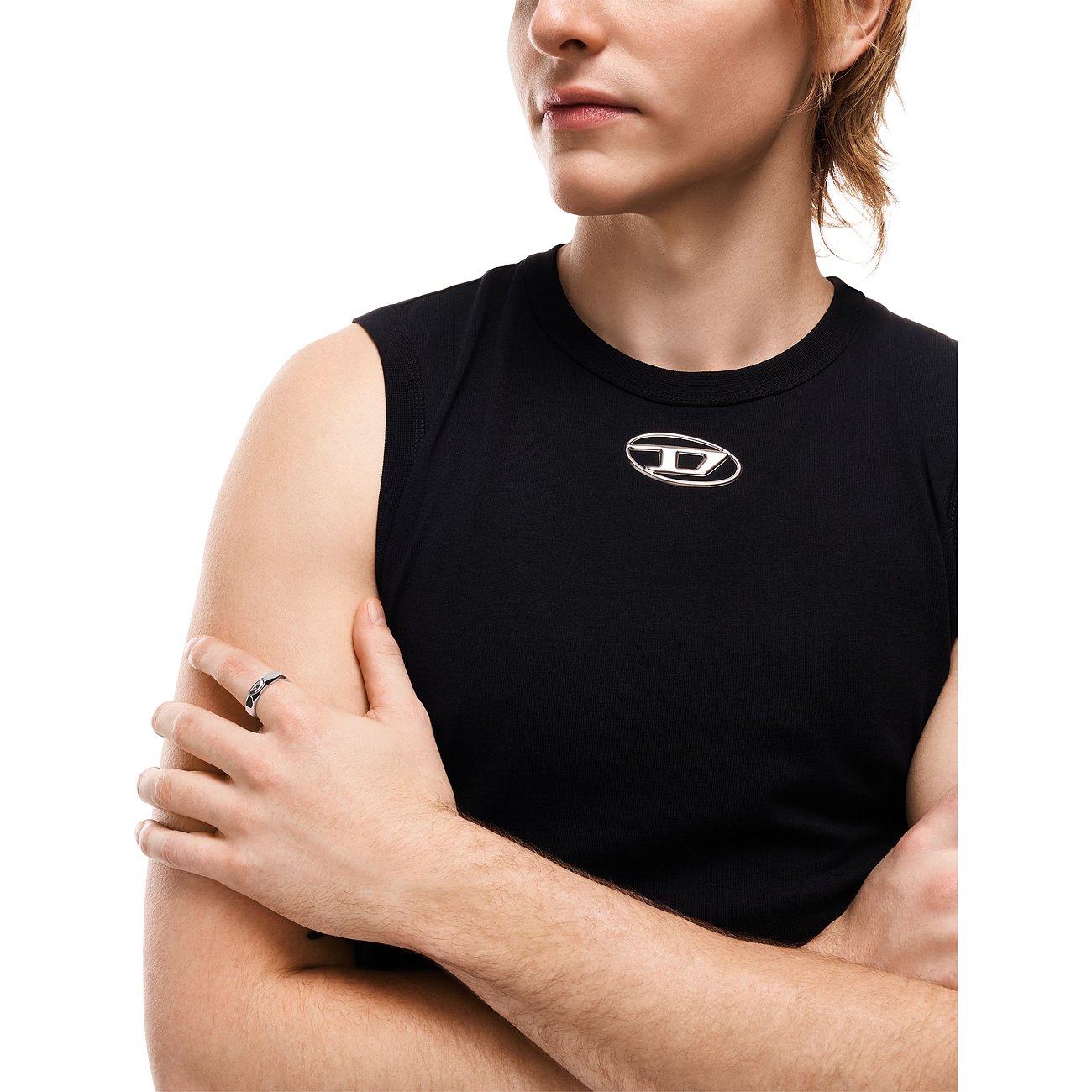 En Diesel-ring af rustfrit stål på hånden af en person med krydsede arme og sort tanktop.