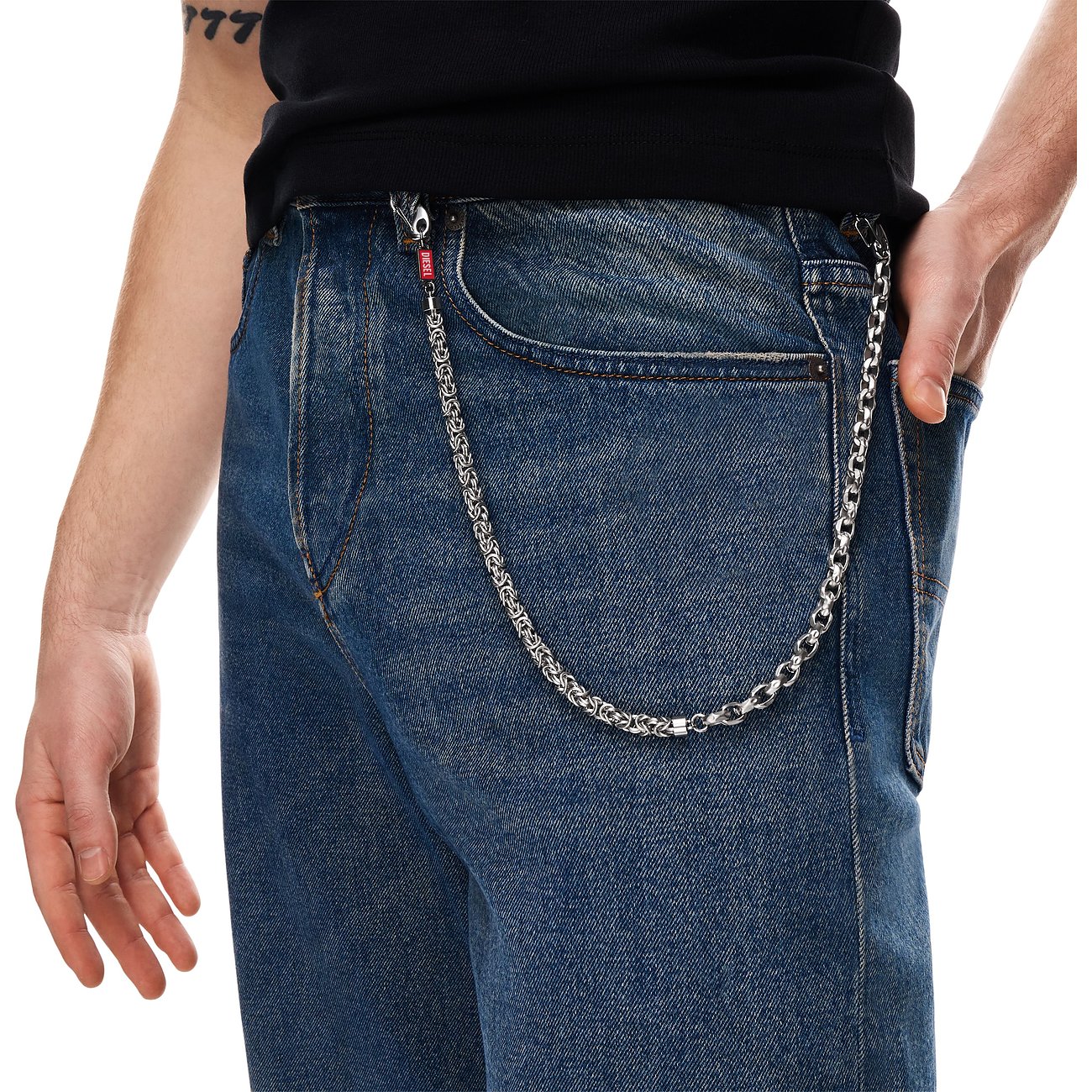 Gros plan d'une hanche masculine avec une chaîne Diesel en acier inoxydable fixée à un jean bleu.