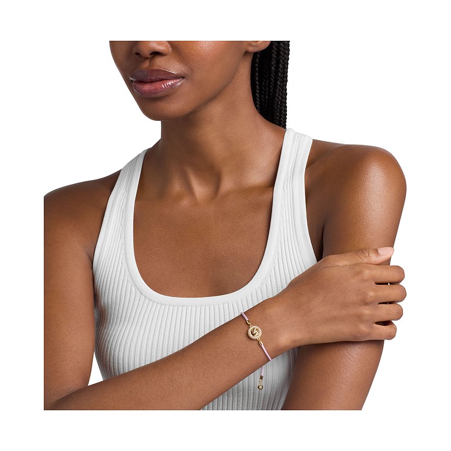 Eine Frau trägt das Michael Kors Armband aus goldfarbenem Metall mit leuchtend pinkem Band und Farbedelsteinen.