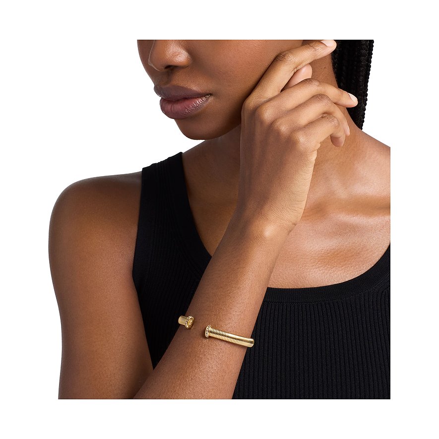 Goldener Michael Kors Armreif am Handgelenk einer Frau, offen in der Mitte, mit viereckigem Zirkonia-Stein links.