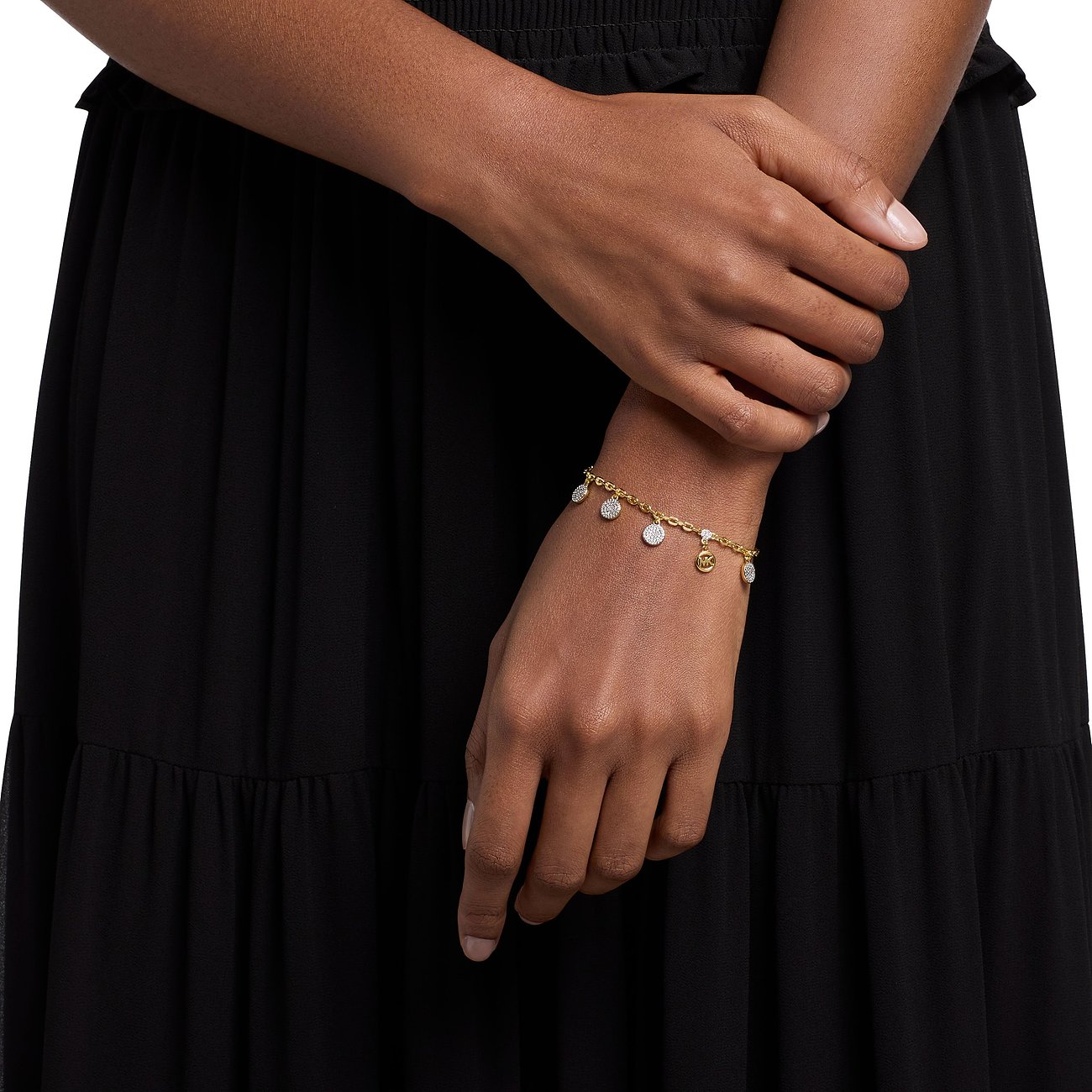 Am Handgelenk einer Person ein goldfarbenes Michael Kors Armband aus Metall mit glitzernden Zirkonia-Anhängern.