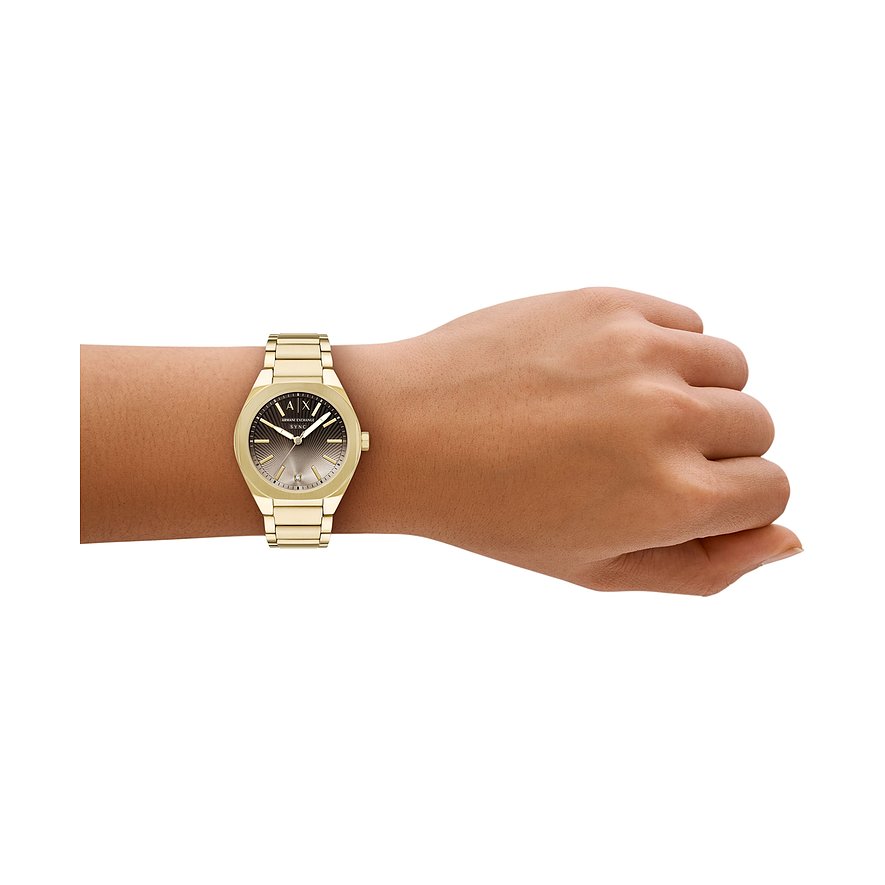 Eine Armani Exchange Damenuhr aus goldfarbenem Edelstahl mit dunkelgrauem Zifferblatt ziert ein Handgelenk.