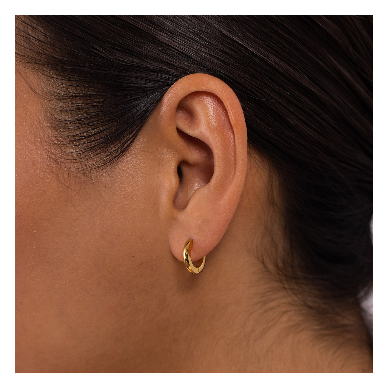 Nahaufnahme eines Ohres mit einem goldenen Creolen-Ohrring aus Edelstahl von Purelei am Ohrläppchen.
