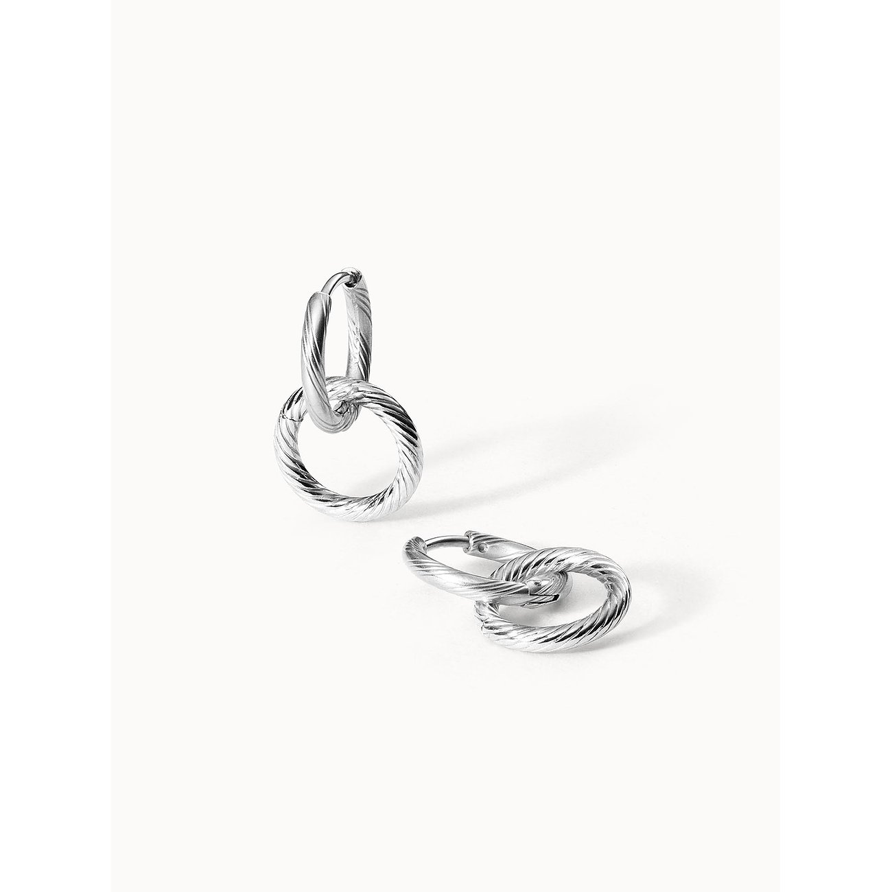 Purelei Ohrschmuck aus Edelstahl mit ineinander verschlungenen, strukturierten Ringen, liegend und stehend.