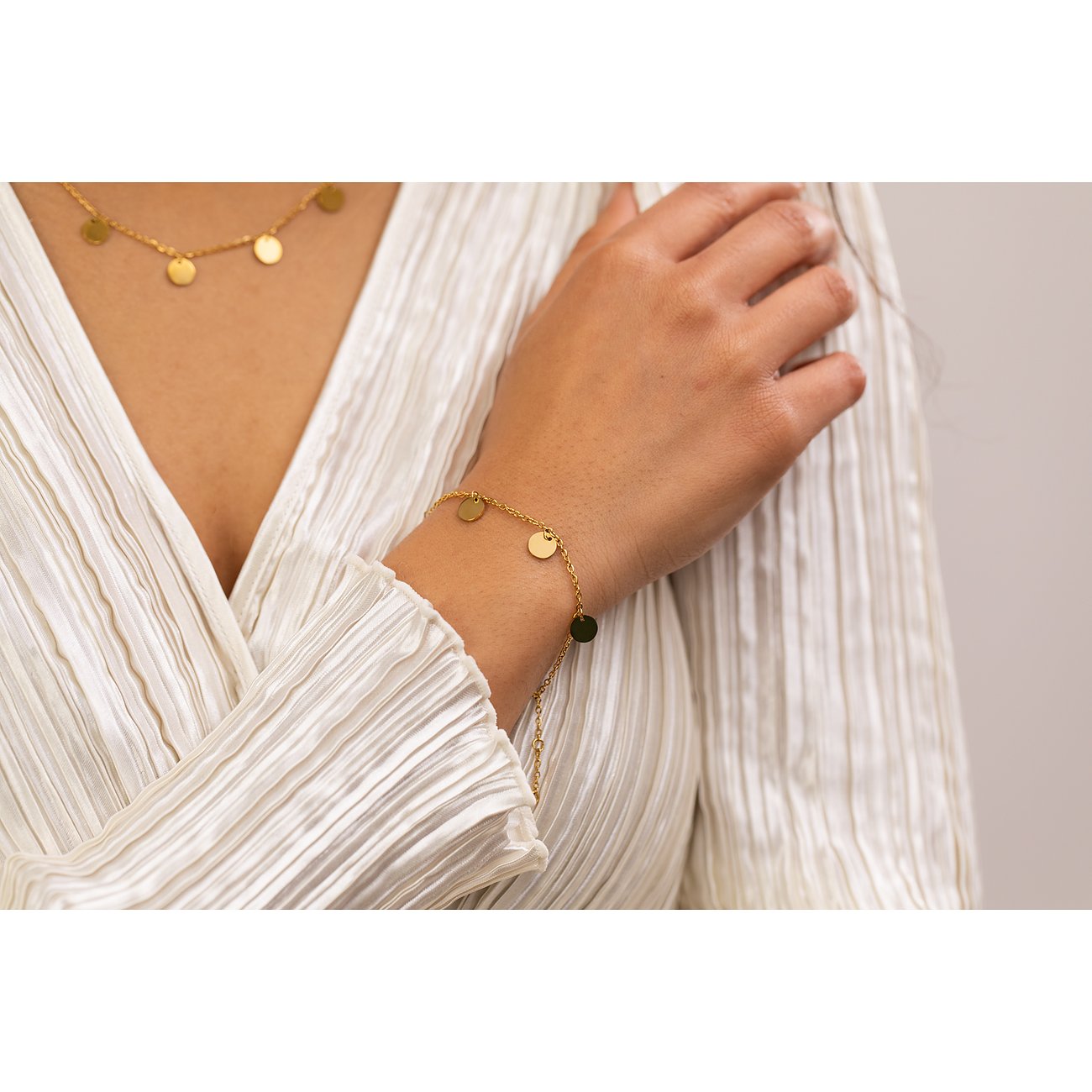 Aan de pols van een vrouw is een Purelei armband te zien, gemaakt van goudkleurig roestvrij staal met ronde hangers.