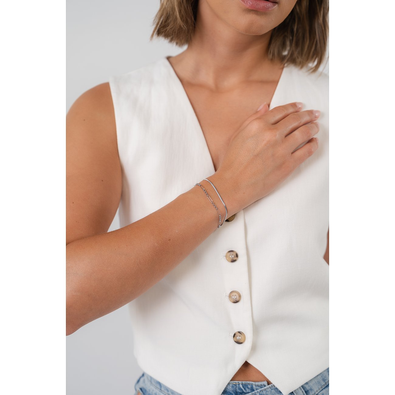 Een vrouw draagt een Purelei roestvrijstalen armband, bestaande uit twee fijne kettingen, elegant om haar pols.