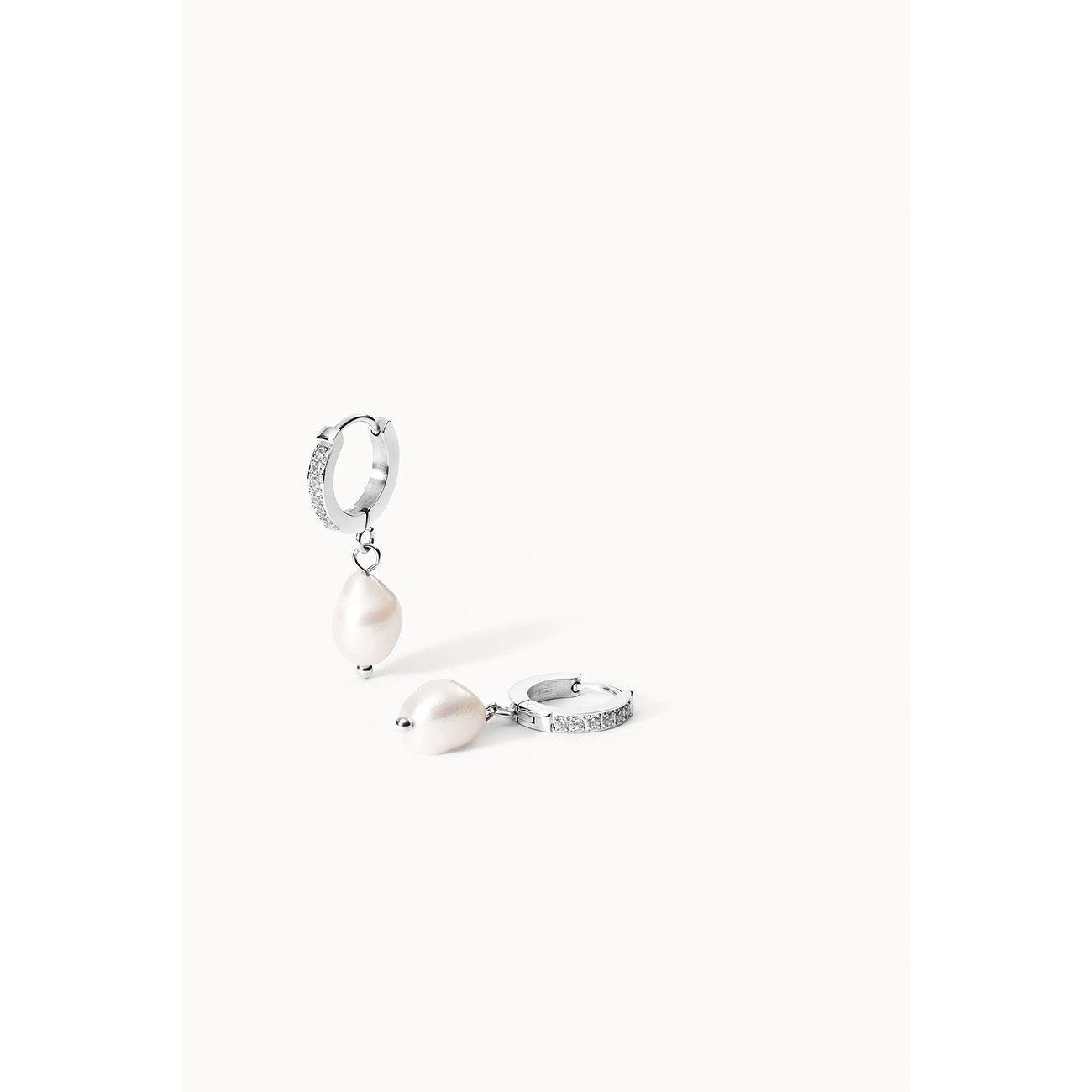 Twee Purelei roestvrijstalen oorhangers met parels, één hangend en één liggend, op een witte achtergrond.