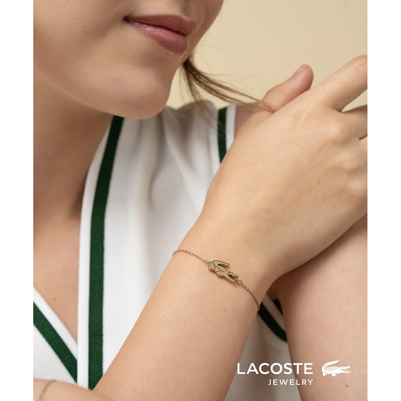 Een vrouw draagt een gouden Lacoste roestvrijstalen armband met krokodilbedel aan een dun kettinkje.