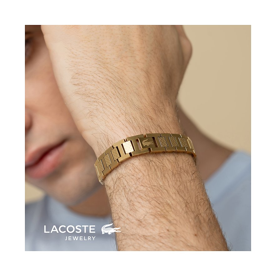 Een gouden Lacoste armband van roestvrij staal. Zichtbaar om de pols van een man op de voorgrond.