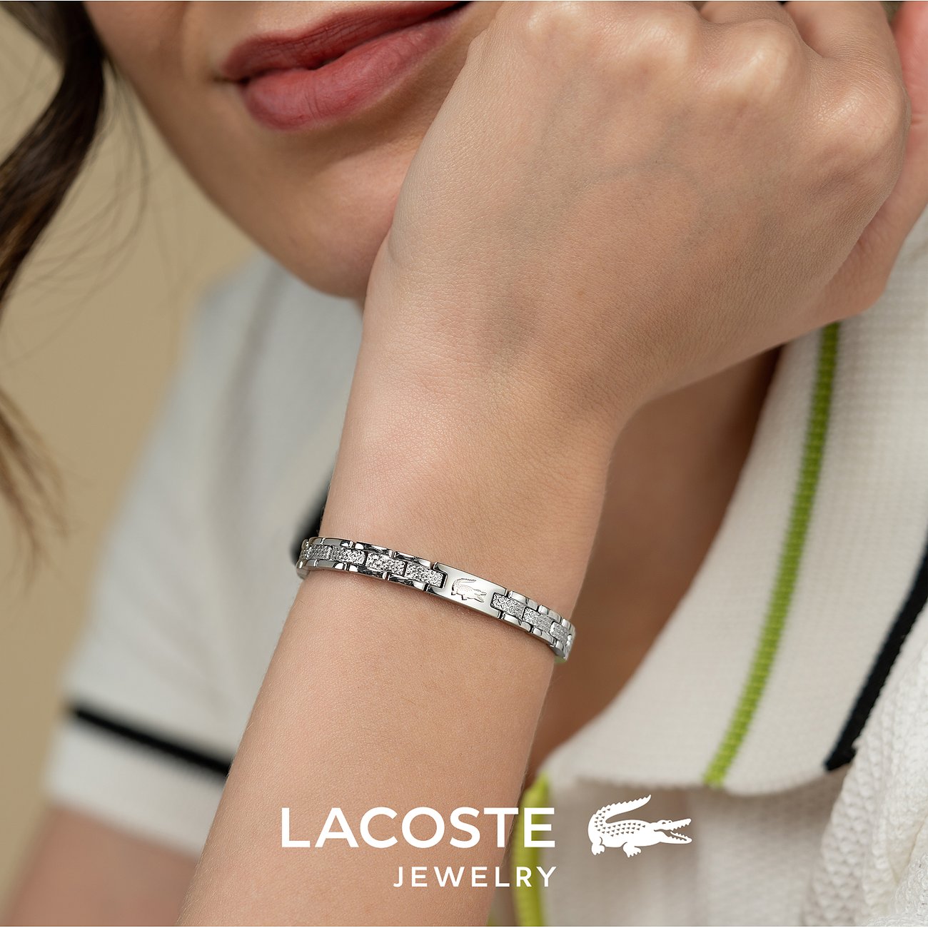 Close-up van een Lacoste roestvrijstalen armband om de pols van een model, met prominent merklogo vooraan.