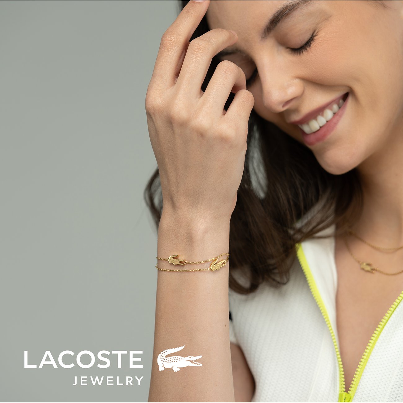Een mooie vrouw draagt een gouden roestvrijstalen Lacoste armband met het kenmerkende krokodillenlogo.