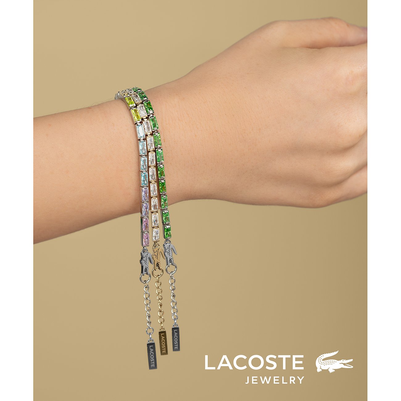 Drie Lacoste armbanden van roestvrij staal met gekleurde zirkonia stenen in diverse groentinten om de pols.