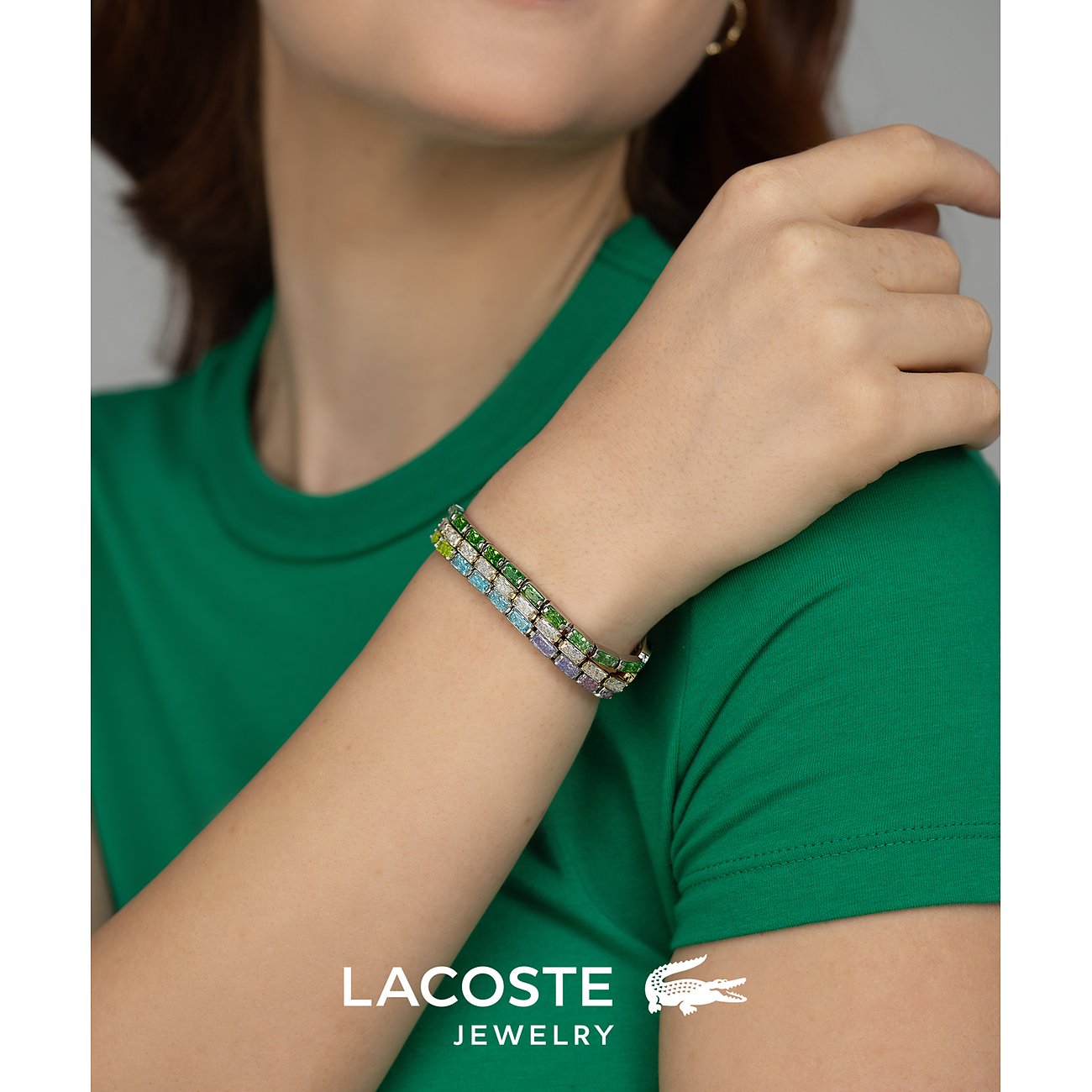 Aan de arm van iemand is een Lacoste armband te zien, van meerrijig roestvrij staal met gekleurde zirkoniasteentjes.