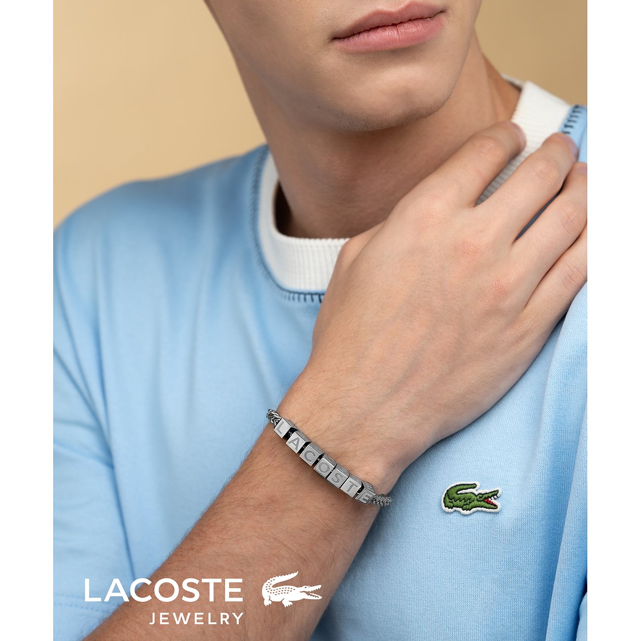 Nahaufnahme eines Mannes, der ein Lacoste Edelstahl Armband mit dem gravierten Schriftzug „Lacoste“ trägt.