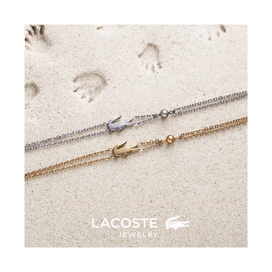 Twee Lacoste roestvrijstalen armbanden op zand. Eén is zilverkleurig, de andere goudkleurig.
