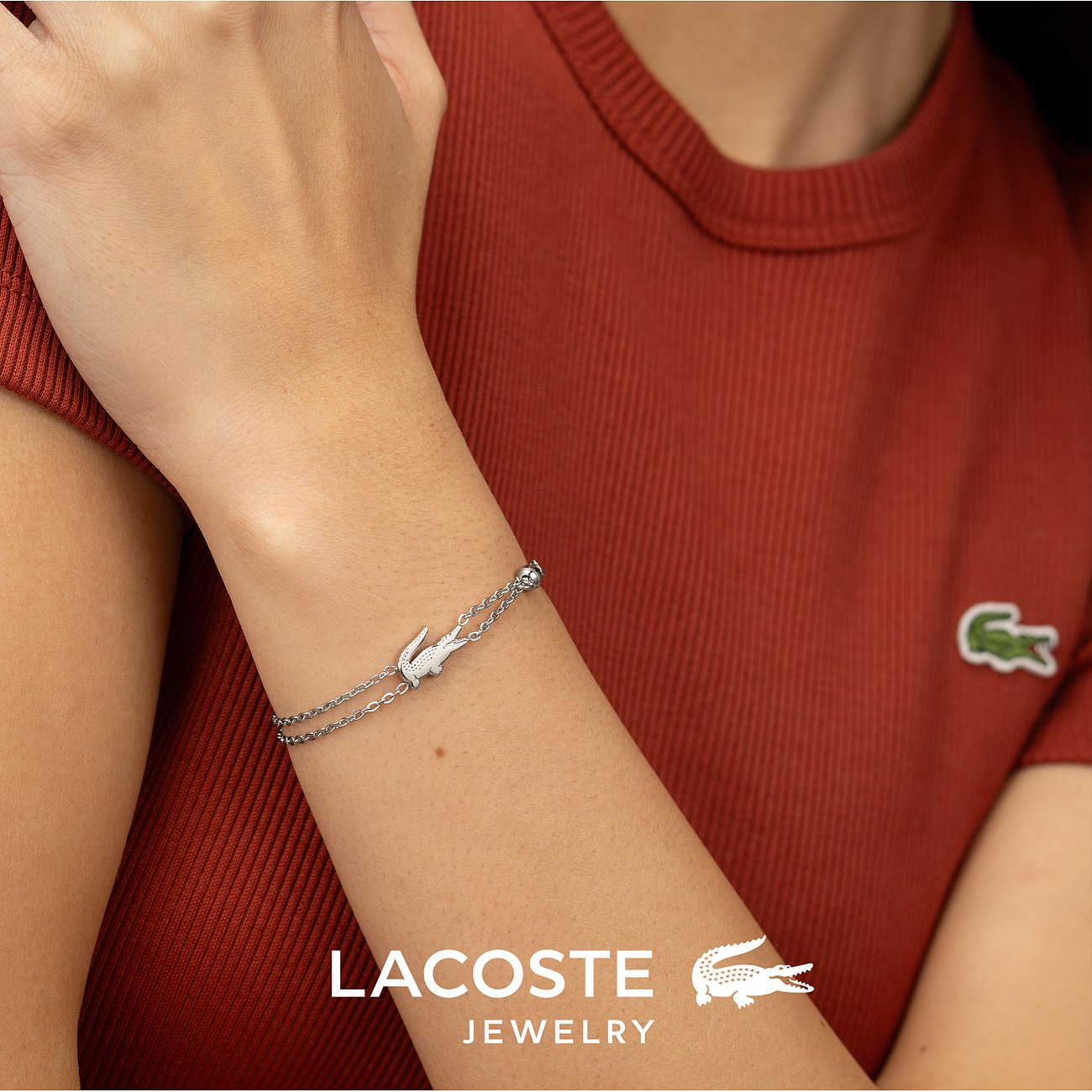 Lacoste armband van roestvrij staal, gedragen om de pols, met een krokodillenbedel en een edelsteen.