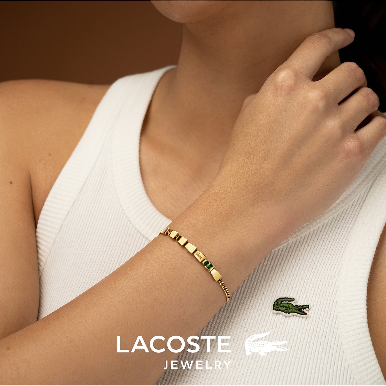 Lacoste armband gedragen om een pols, van goudkleurig roestvrij staal met groene kristallen kleurstenen.