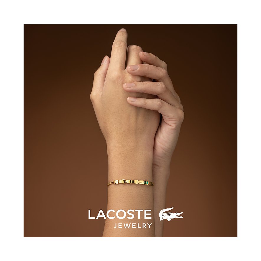 Een gouden Lacoste roestvrijstalen armband met groene kristalaccenten, gedragen om een pols.