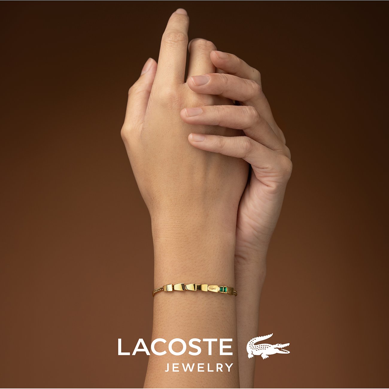 Een gouden Lacoste roestvrijstalen armband met groene kristalaccenten, gedragen om een pols.