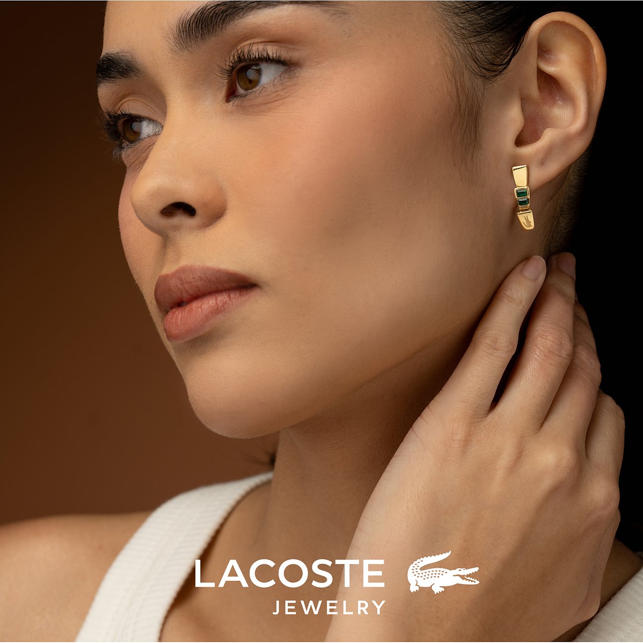 Nahaufnahme einer Frau, die einen Lacoste-Ohrring aus goldfarbenem Edelstahl mit grünen Kristall-Farbsteinen trägt.