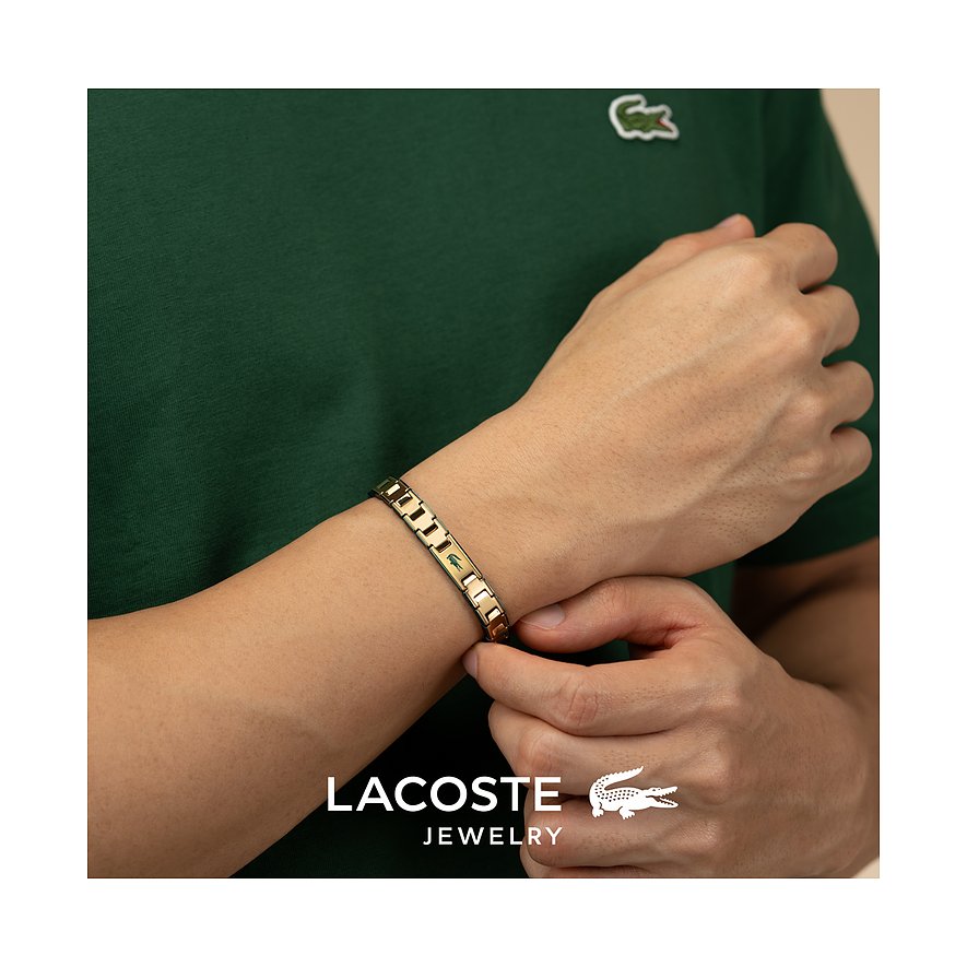 Close-up van een gouden Lacoste roestvrijstalen armband om de pols van een man met een groen shirt.