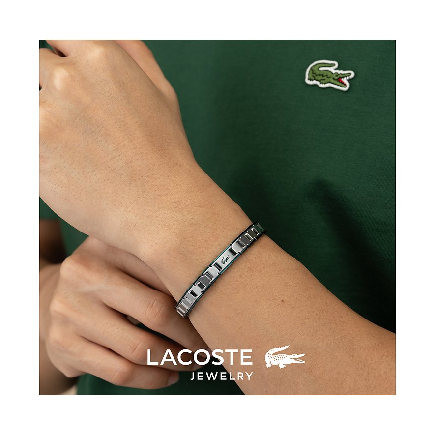 Een Lacoste armband van roestvrij staal, gedragen om een pols, met het krokodillenlogo op het middendeel.